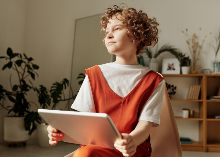 Photo of child sitting on chair while holding tablet